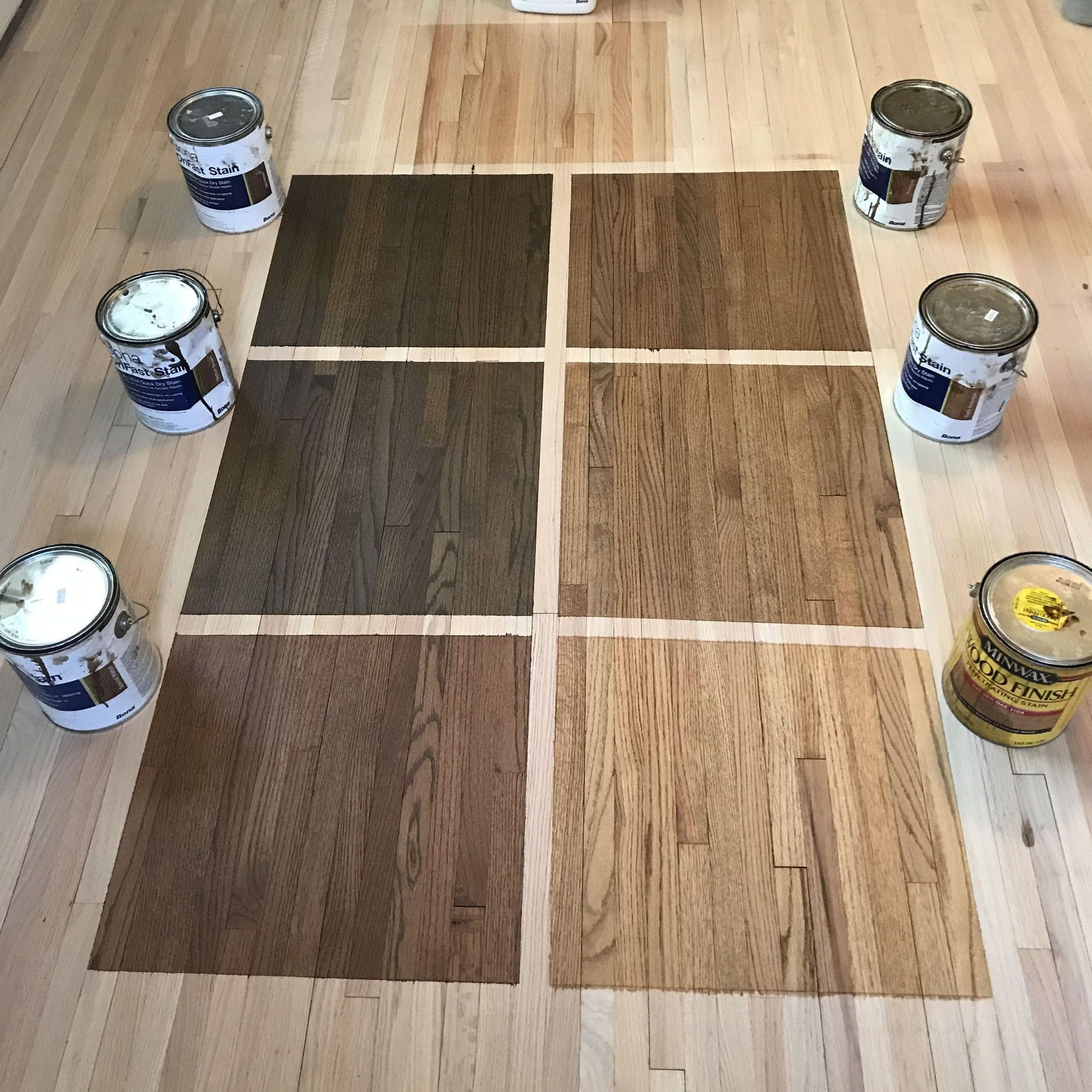 Stained wood samples on hardwood floor, surrounded by stain cans, showcasing color options.