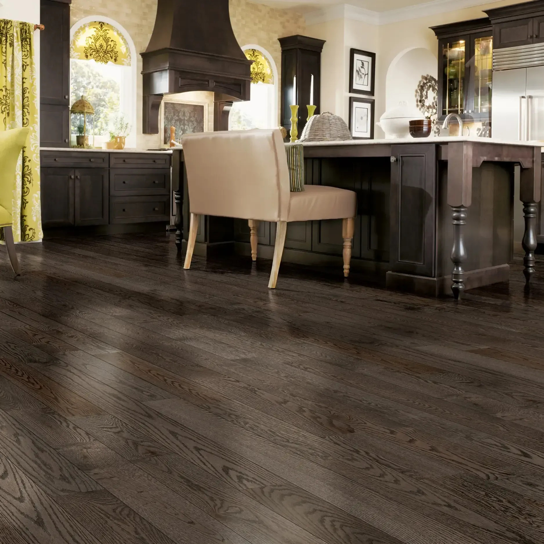 Dark wood kitchen floor in front of a kitchen island with seating. Dark cabinets and vent hood in background.