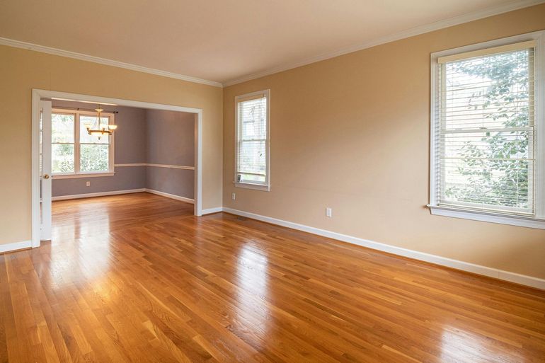 Empty room with wood floors and three windows, doorway to another room.
