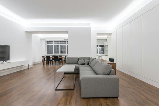 Modern, minimalist living room with gray sectional sofa, wood floors, white walls, and built-in storage.