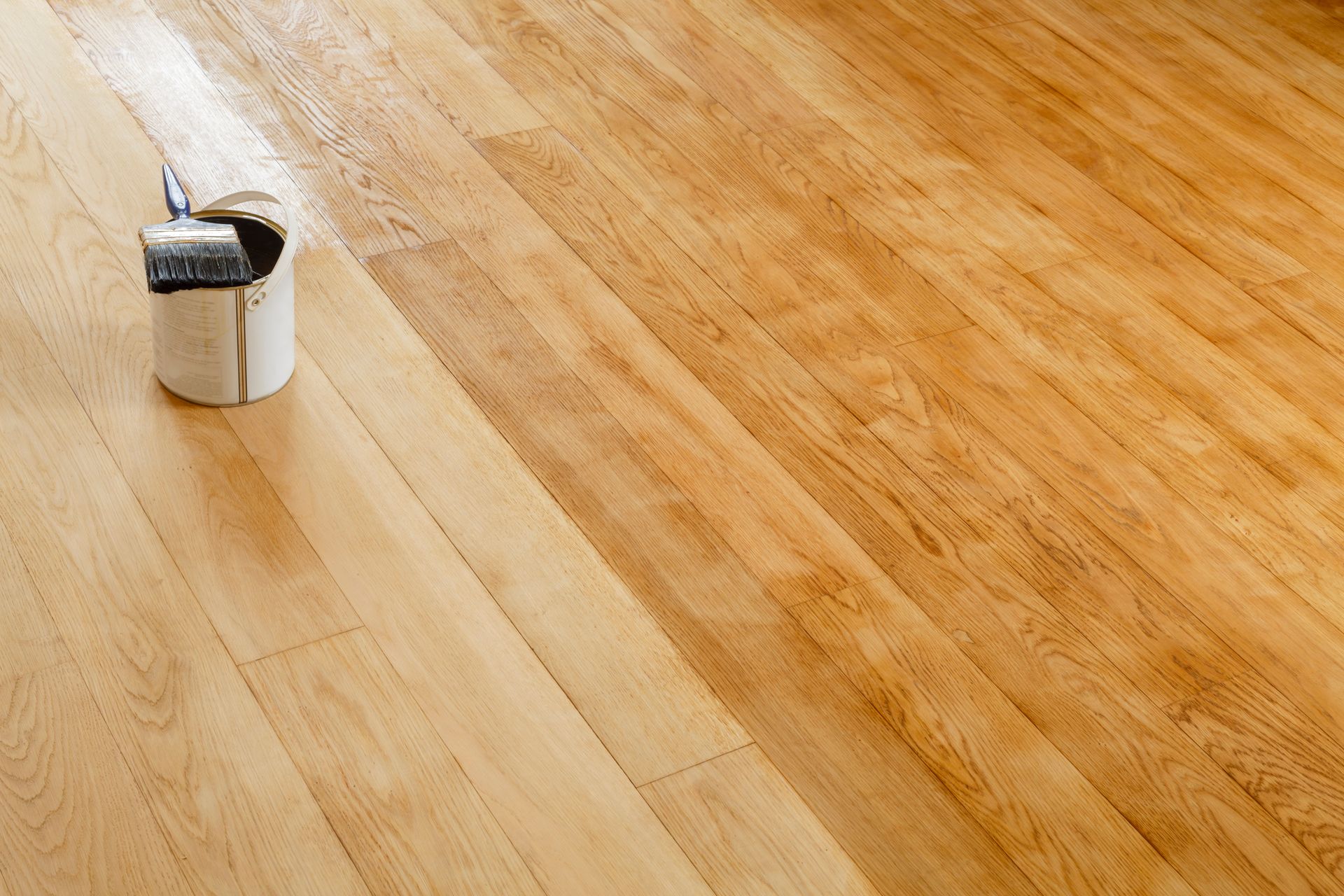 Close-up of a small paint can and roller on a light wooden floor.