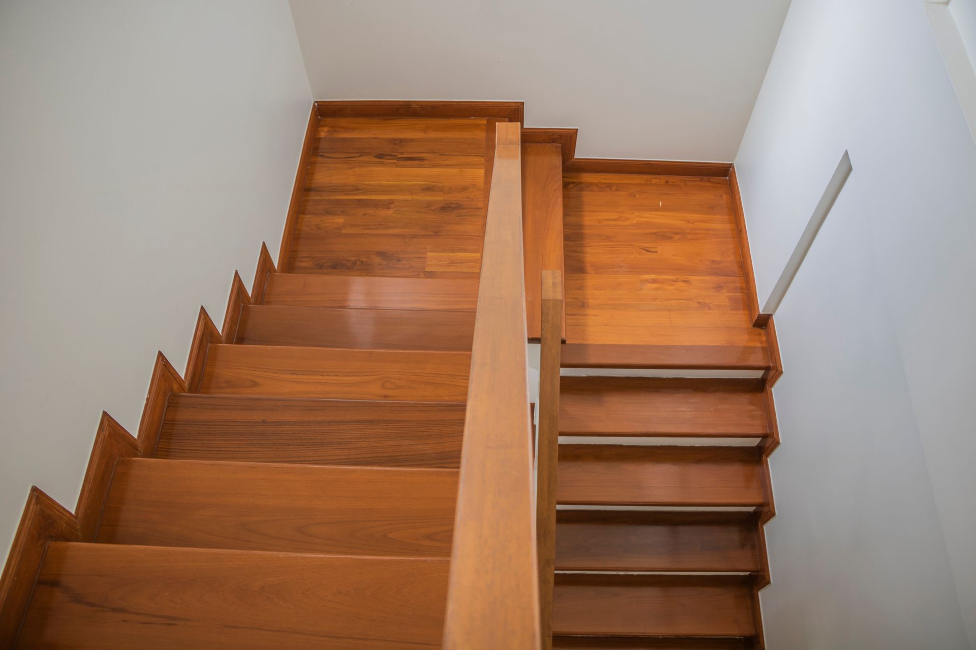 Wooden staircase with two flights and a central landing in a white-walled interior.