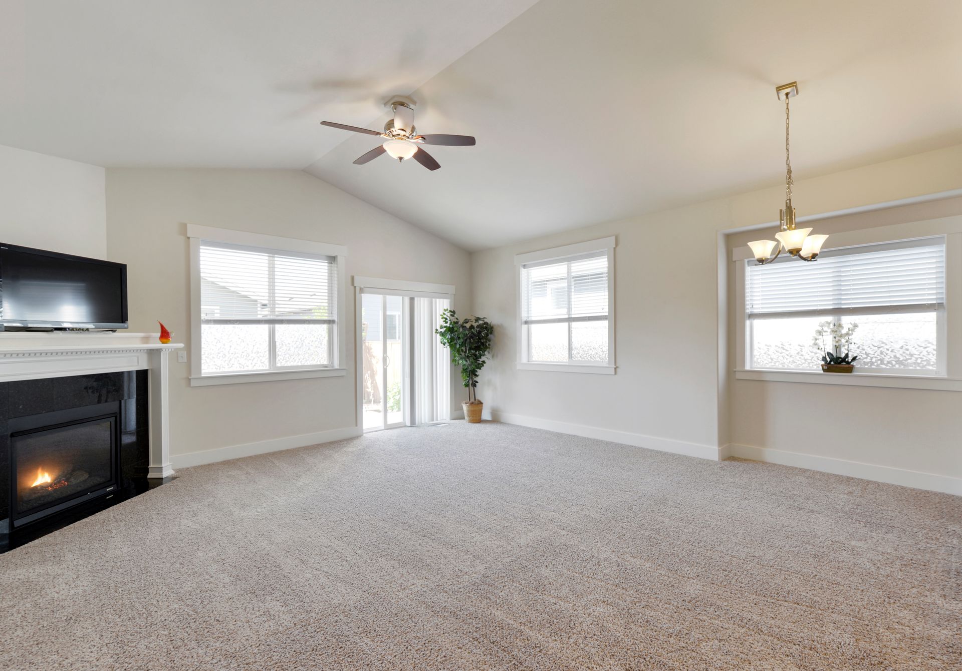 Spacious carpeted living room with fireplace, ceiling fans, large windows, and light neutral walls