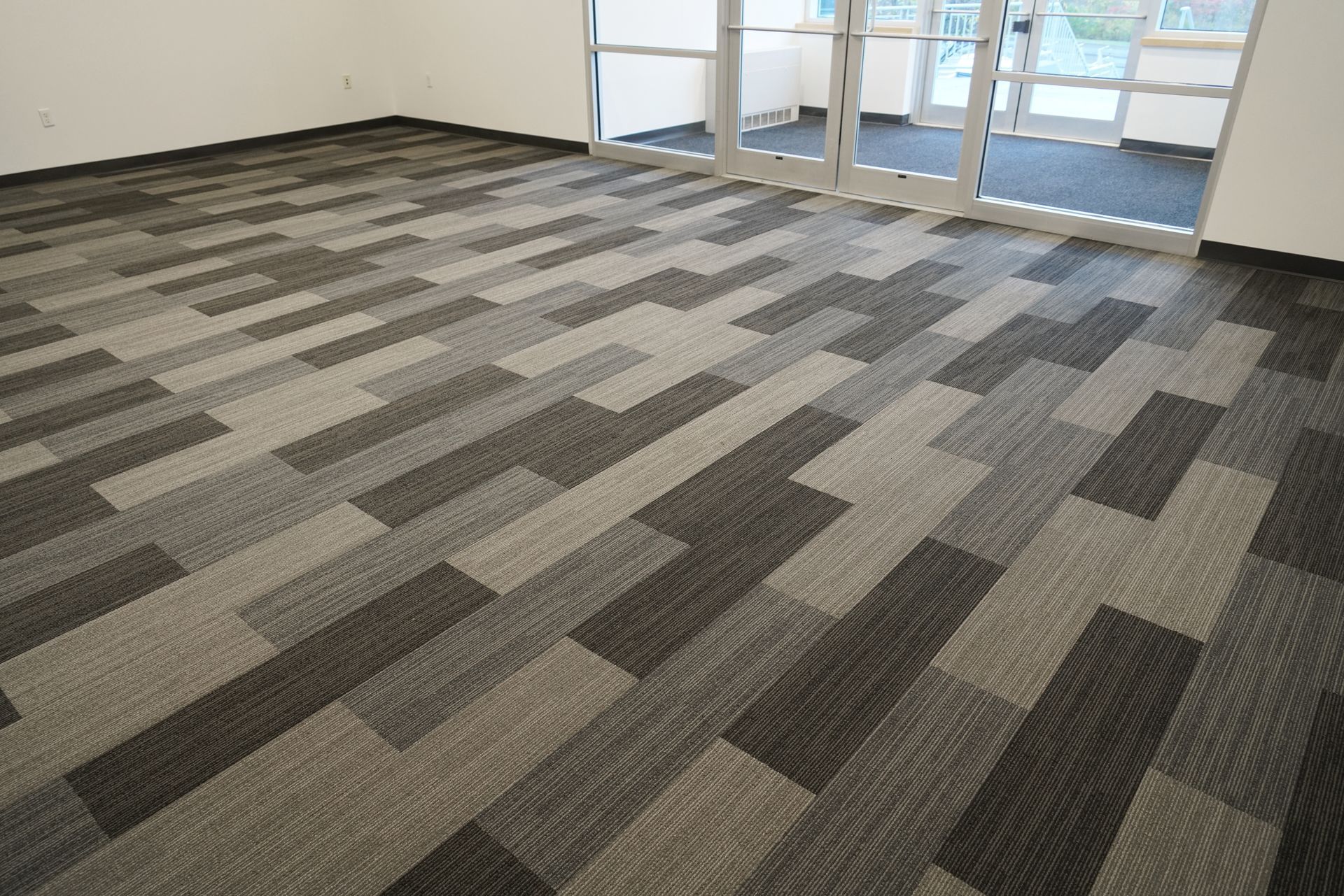 Empty office room with gray patterned carpet and glass doors at the back