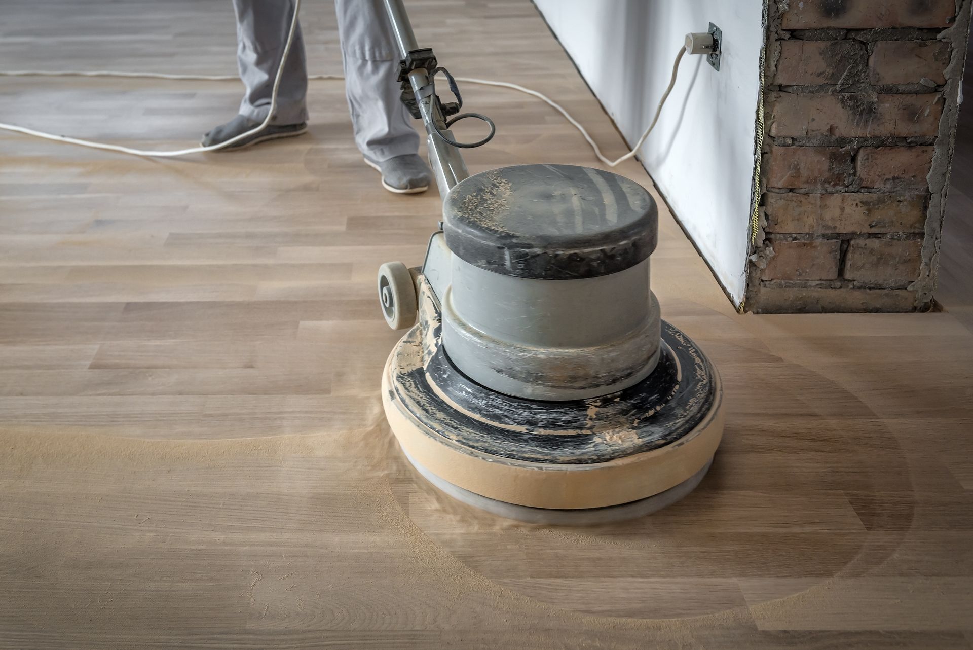 Floor sander grinding a wooden floor, leaving a smooth finish and dust around the machine.
