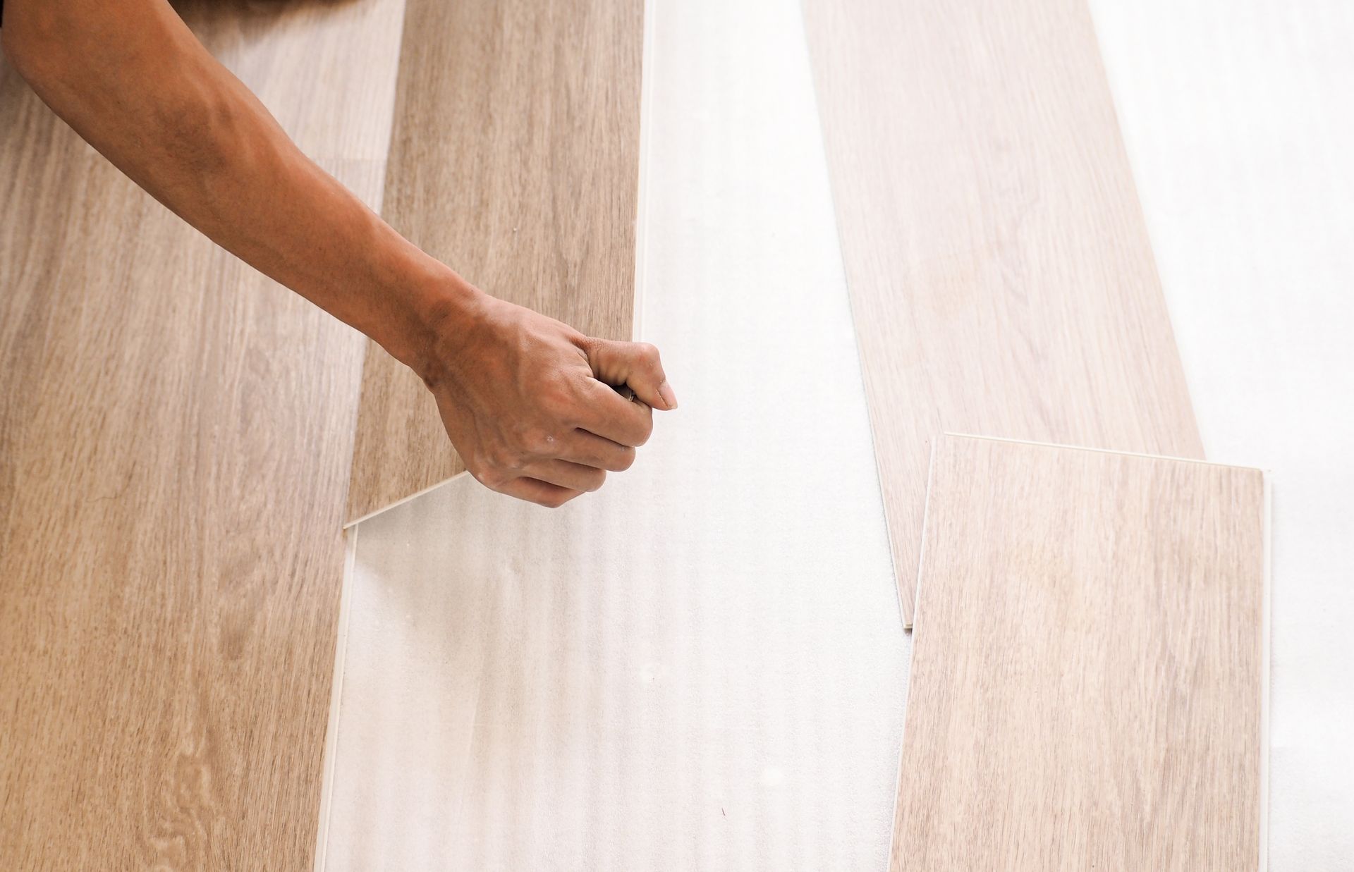 Hand peeling back a white protective sheet from a light wood floor board sample