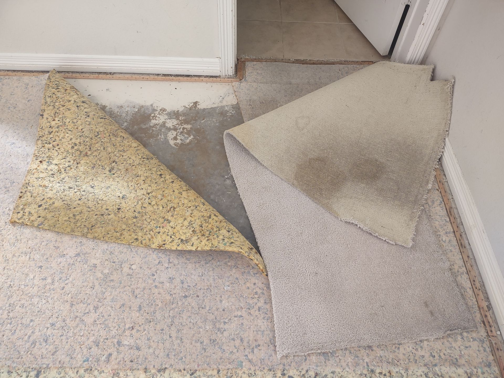 Two torn carpet tiles on a floor near a doorway, one beige and one light gray.