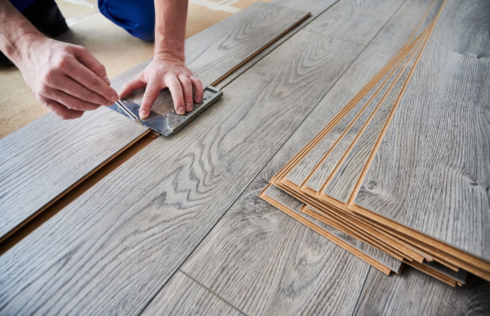 A person using a carpenter’s square and pencil to measure and mark grey wood-look laminate flooring planks.