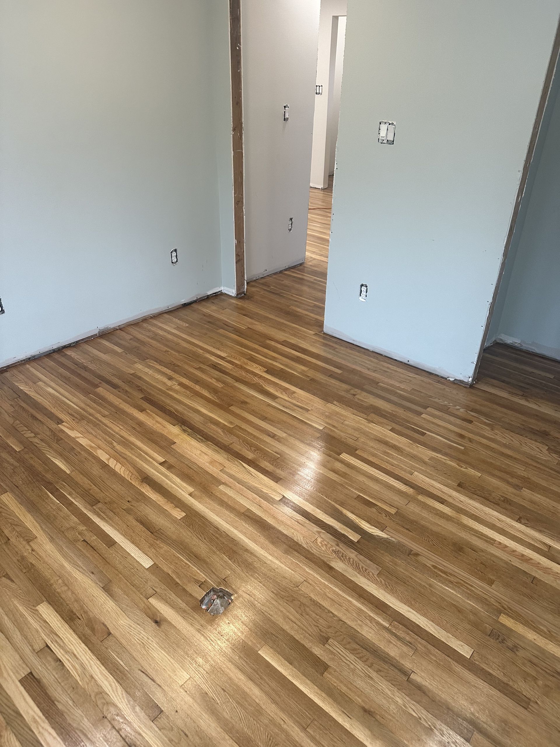 Empty room with glossy wood floors, light gray walls, and an open doorway.