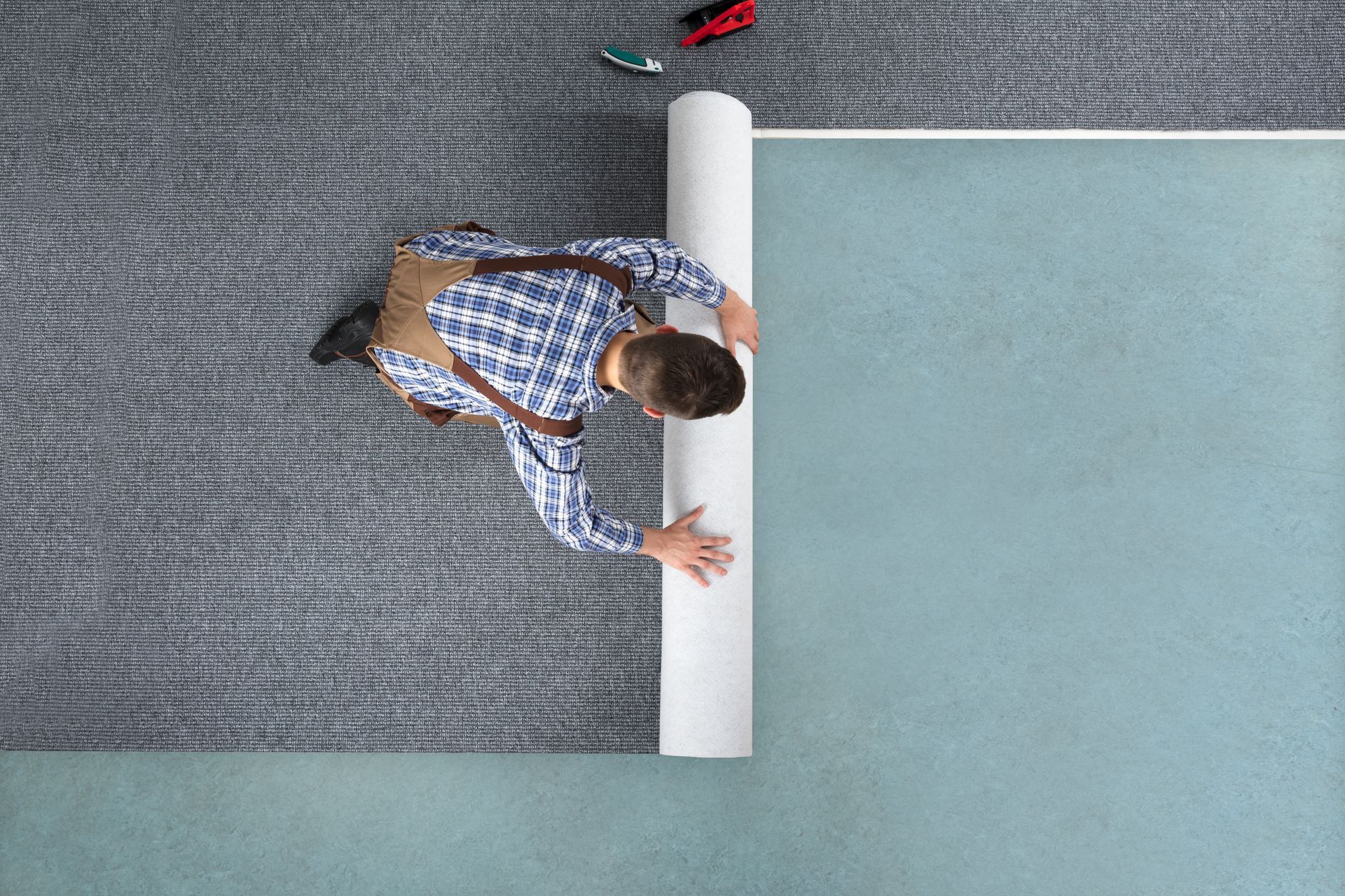 Person stretching on a gray carpet beside a pale blue mat, seen from above.