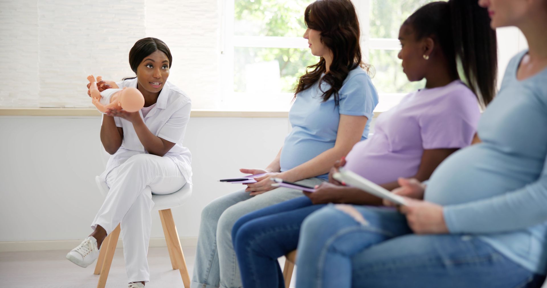 A healthcare worker demonstrates with a fetal model to a group of pregnant women seated in a room.