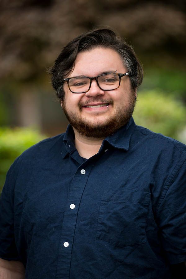 Man with glasses, smiling, in navy blue shirt, outdoors.