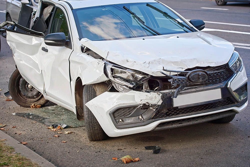 White car with severe front-end and side damage on a city street.