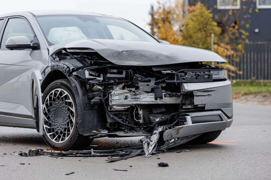 Damaged gray car after a collision, front end destroyed, debris on the road.