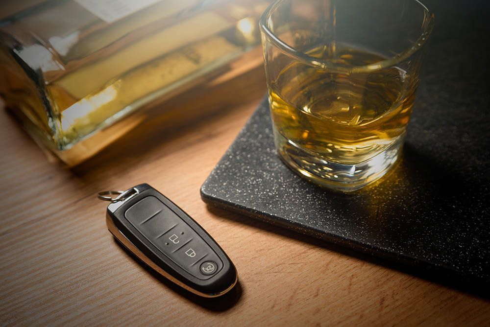 Car keys next to a glass of whiskey and a liquor bottle on a wooden surface.