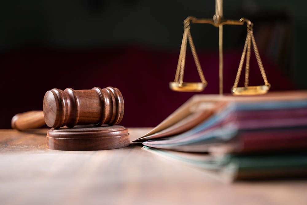 Wooden gavel on a stand next to scales of justice and stacked law books on a desk.