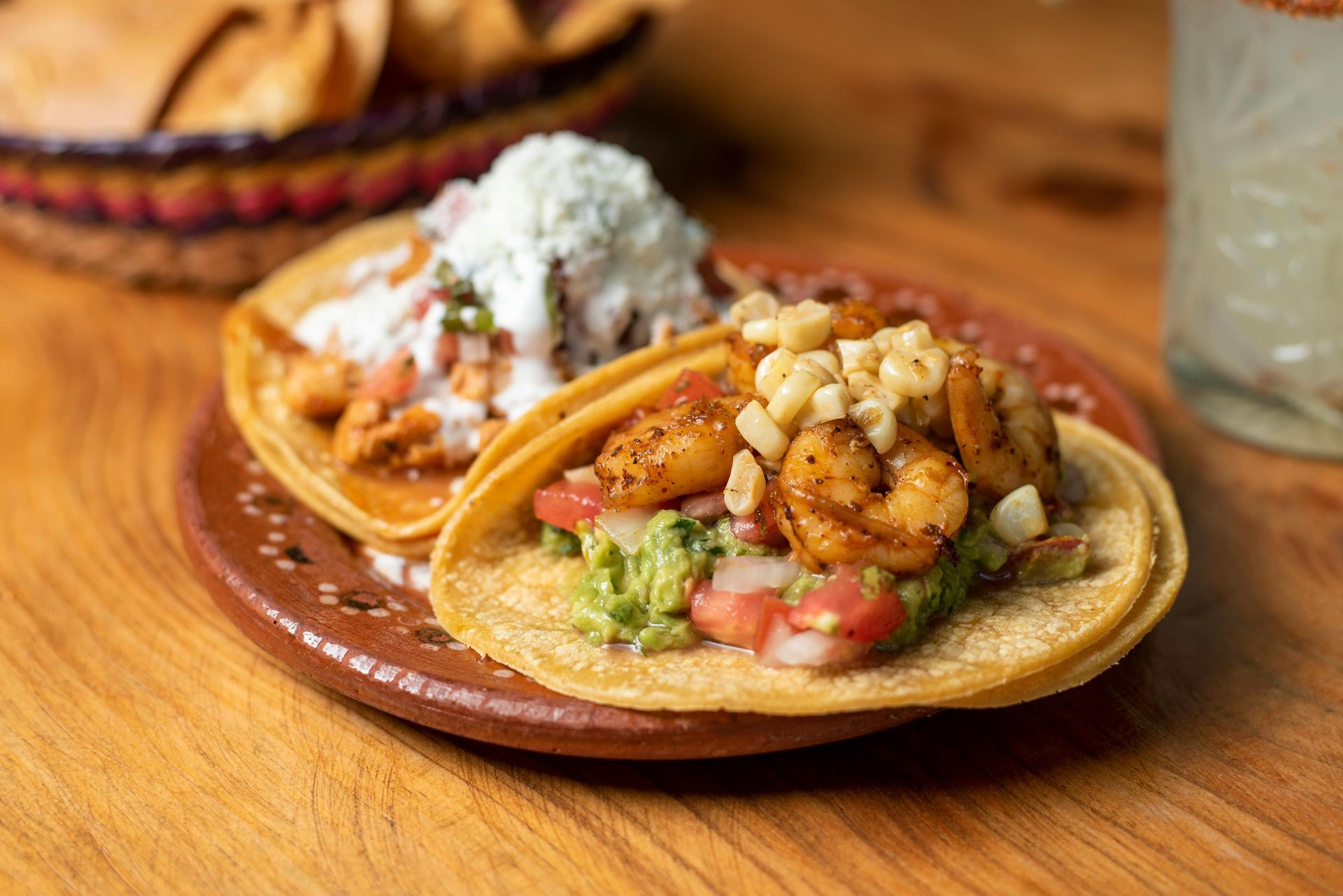 Two tacos on a wooden table, one topped with cheese and the other with shrimp and lettuce