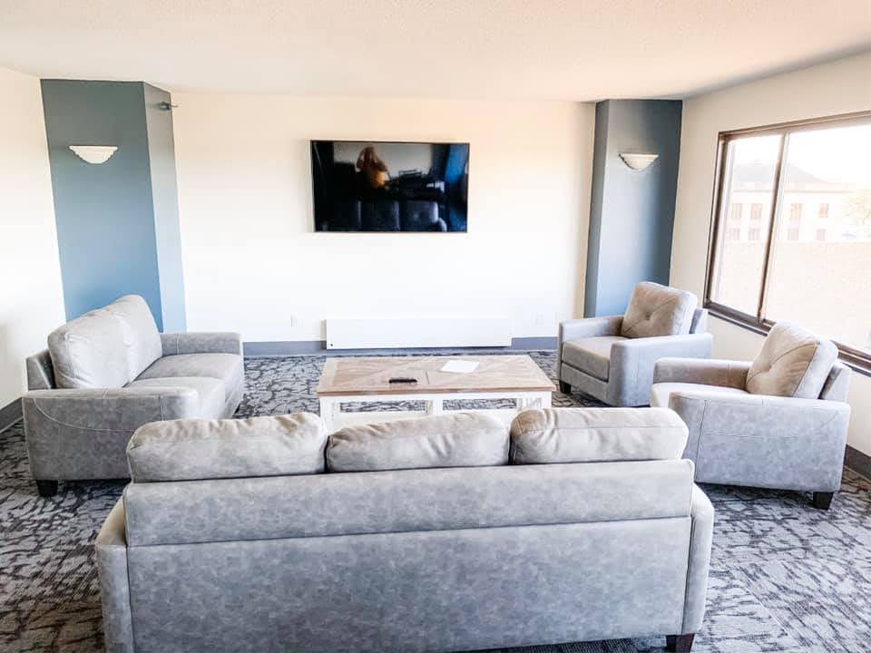 Interior view of community center with three grey couches, coffee table, and flat screen television.