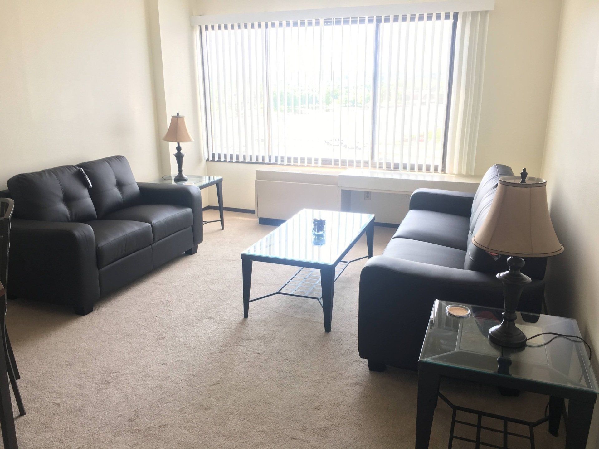 Interior view of living room example with light gray carpet, two brown leather couches glass coffee table, and large window.