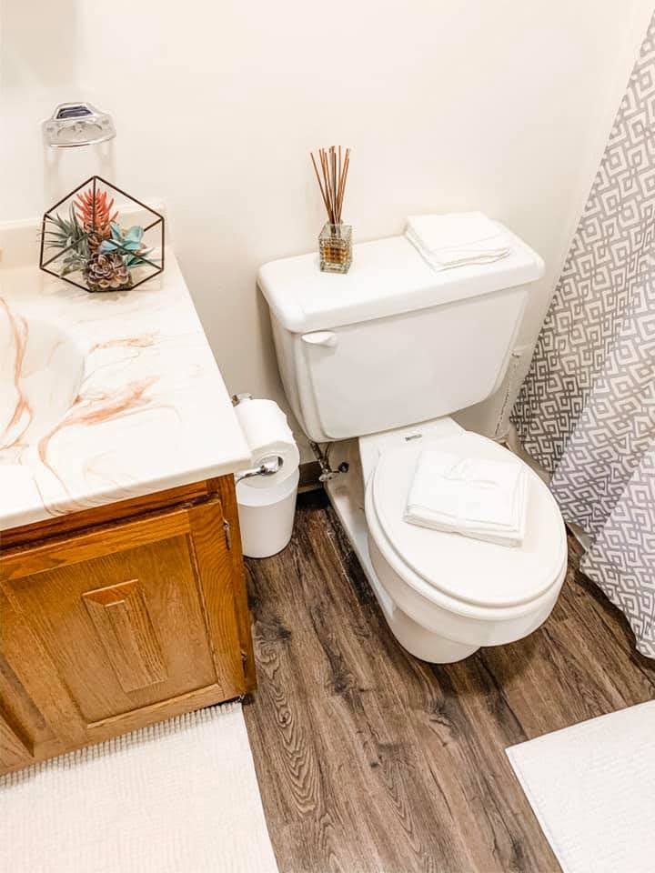 Bathroom example with sink vanity with light wood cupboards, toilet, white towels, shower curtain.