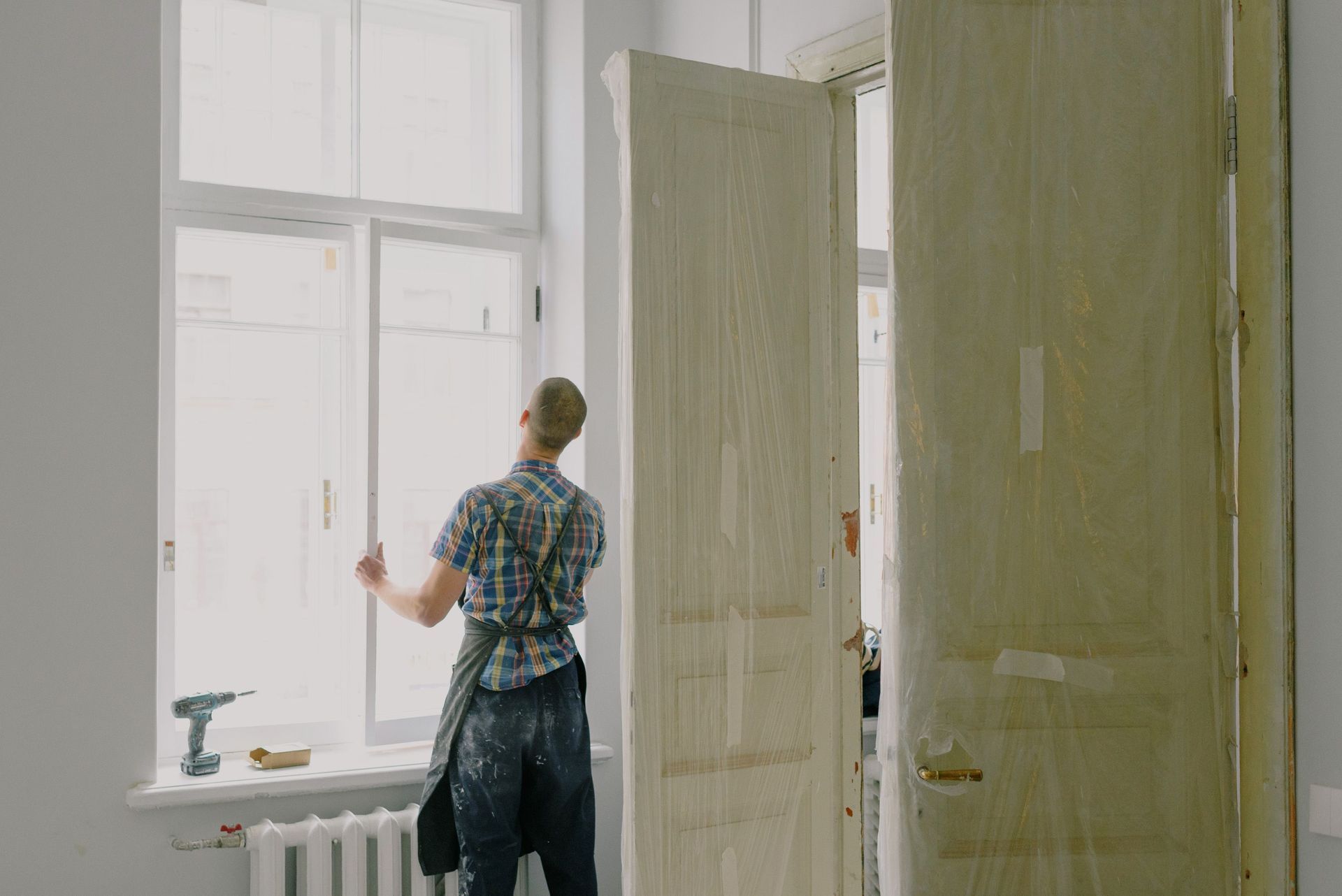 Person painting a wall in a bright room with large windows and a partially covered door