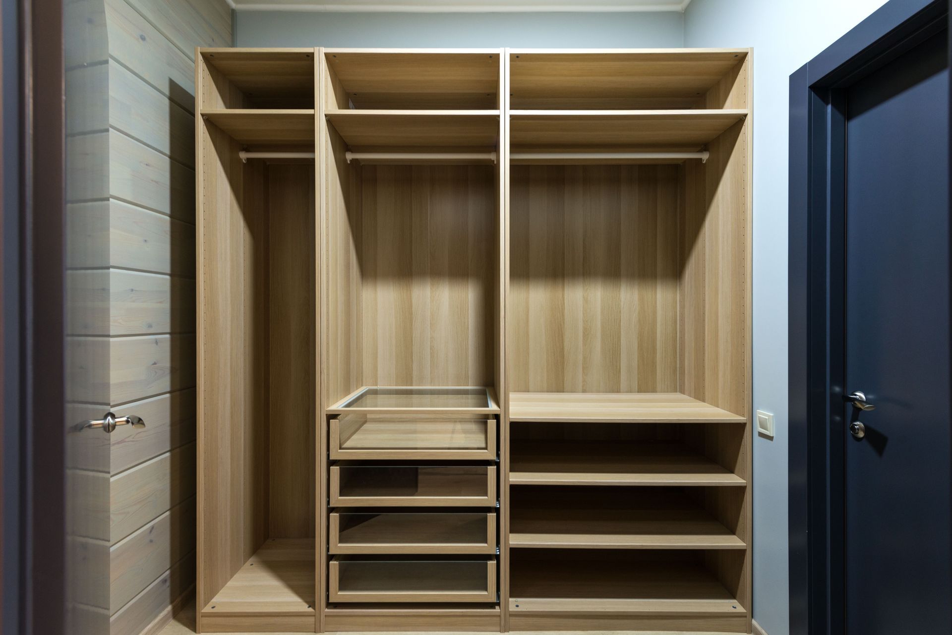 Empty wooden walk-in closet with shelves, drawers, and hanging rods in a modern hallway