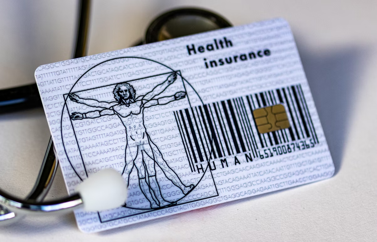 Health insurance card with a barcode, microchip, and Vitruvian Man design, resting on a stethoscope.