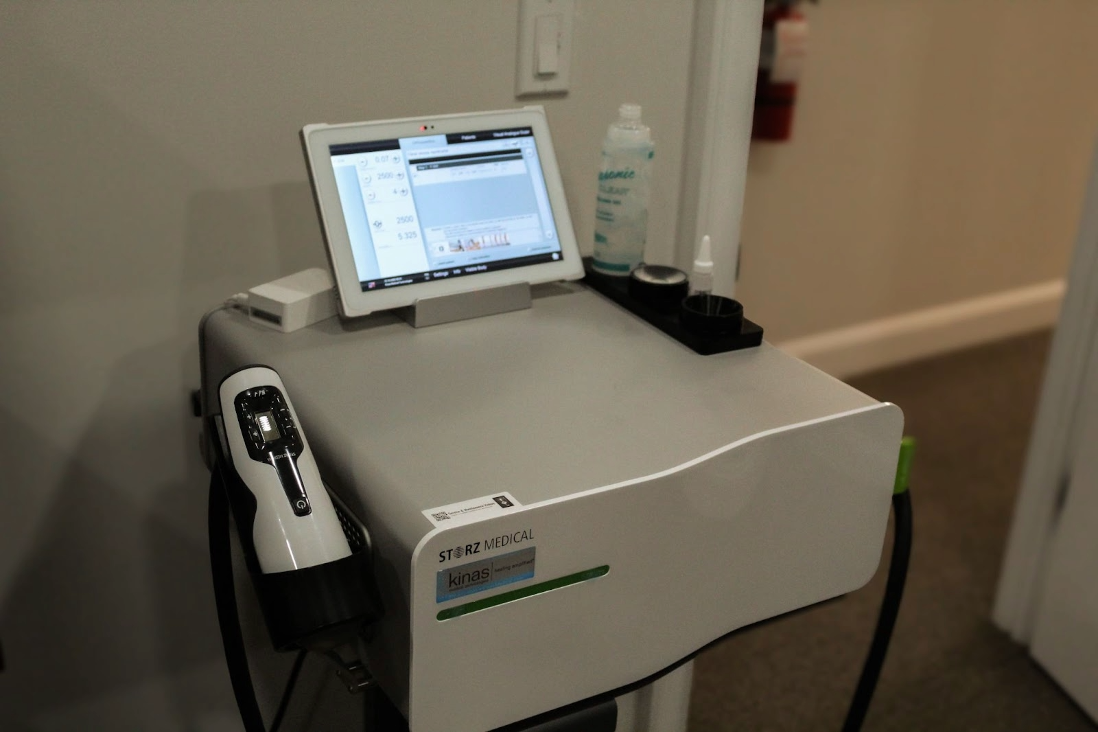 Medical device with a tablet display and hand piece, likely for aesthetic treatments, in a clinic setting.