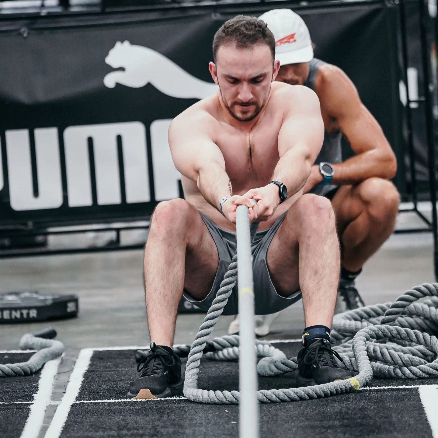 Man doing battle rope exercise at a gym, another person observes, Puma logo in background.