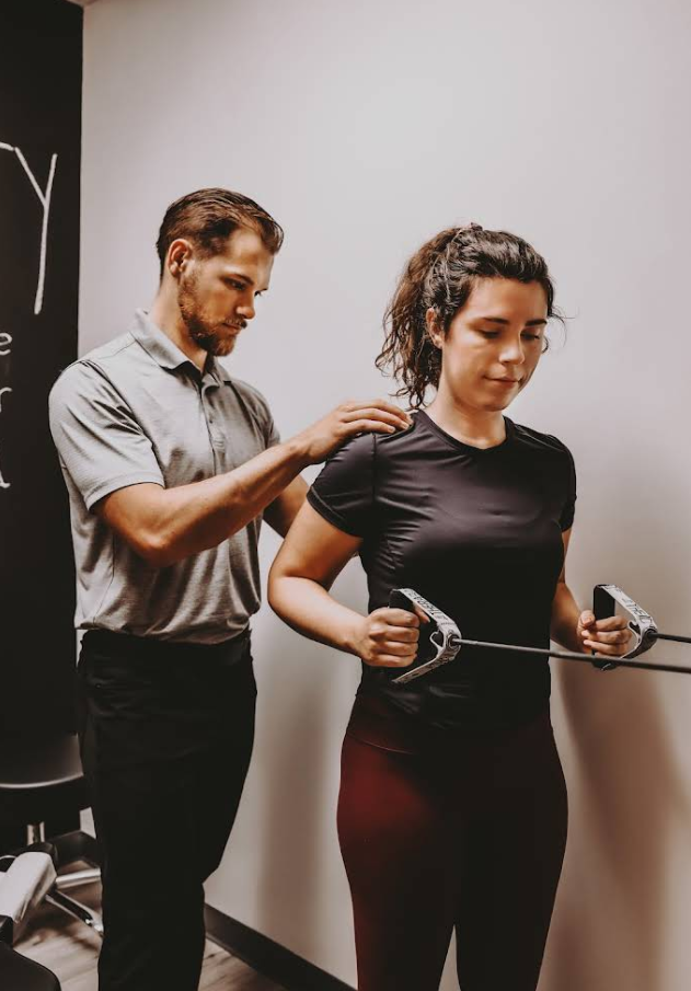Man assisting woman with a resistance band exercise in a clinic.