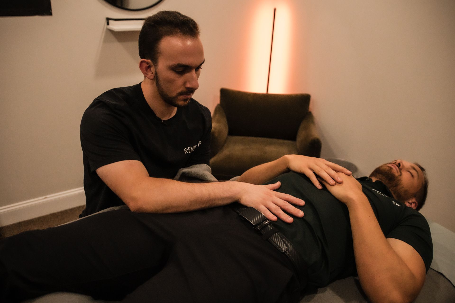 A man giving a massage to another man's back in a gym setting.