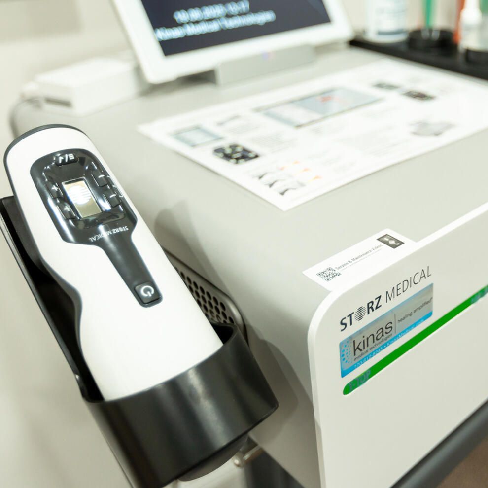 A white and black medical device on a stand, possibly for a clinic, with a tablet in the background.