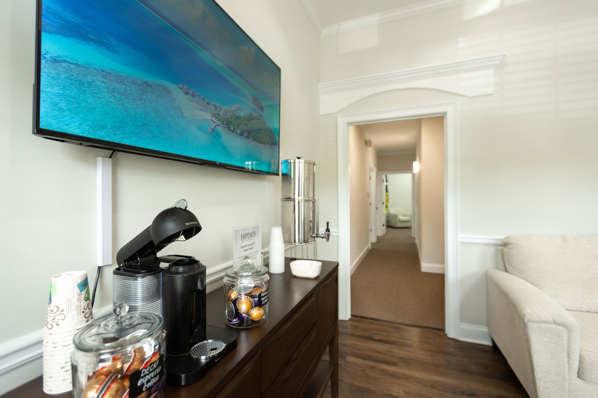 Coffee station and waiting area with TV and hallway entrance.