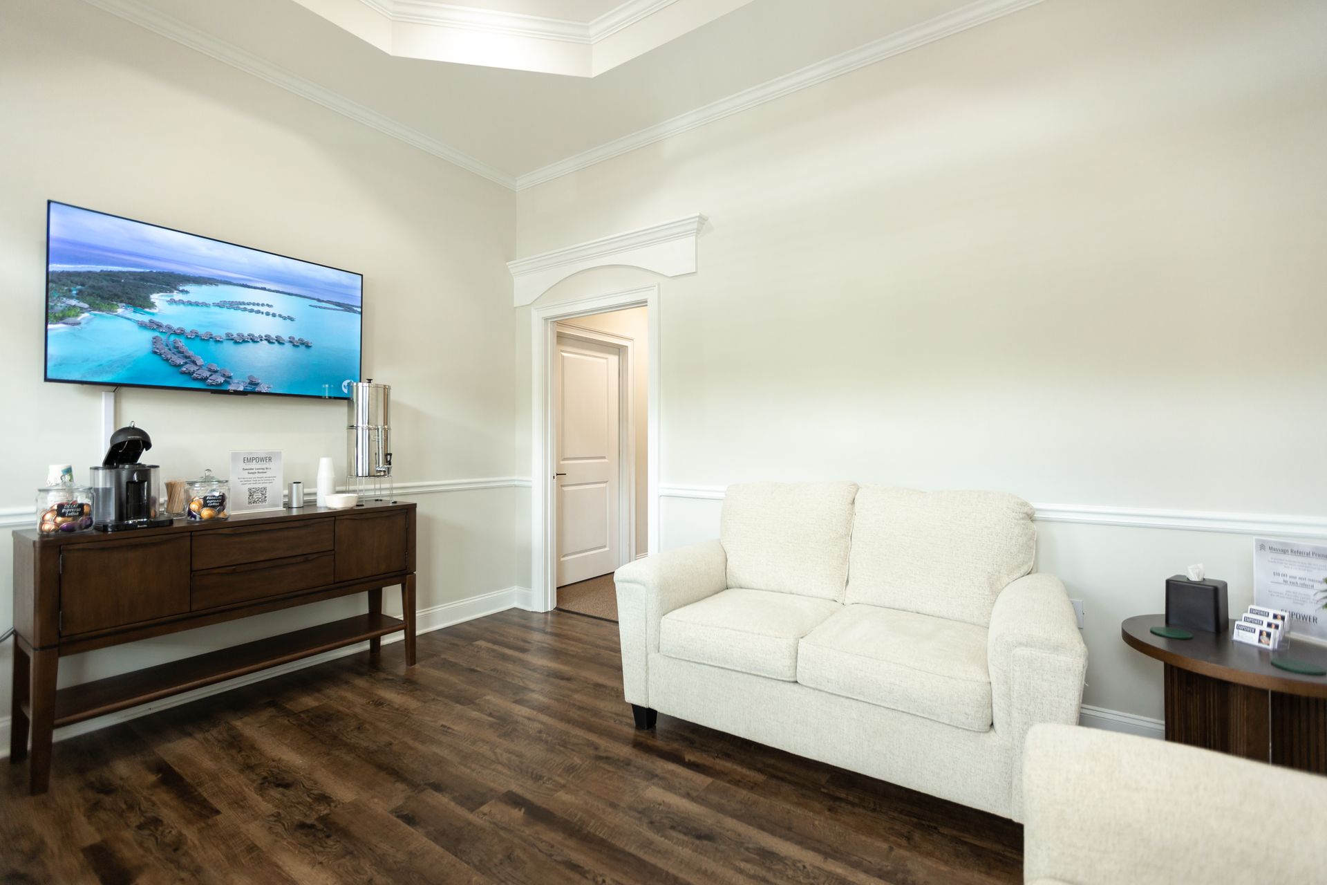 Waiting room with white walls, sofa, TV, and coffee station.