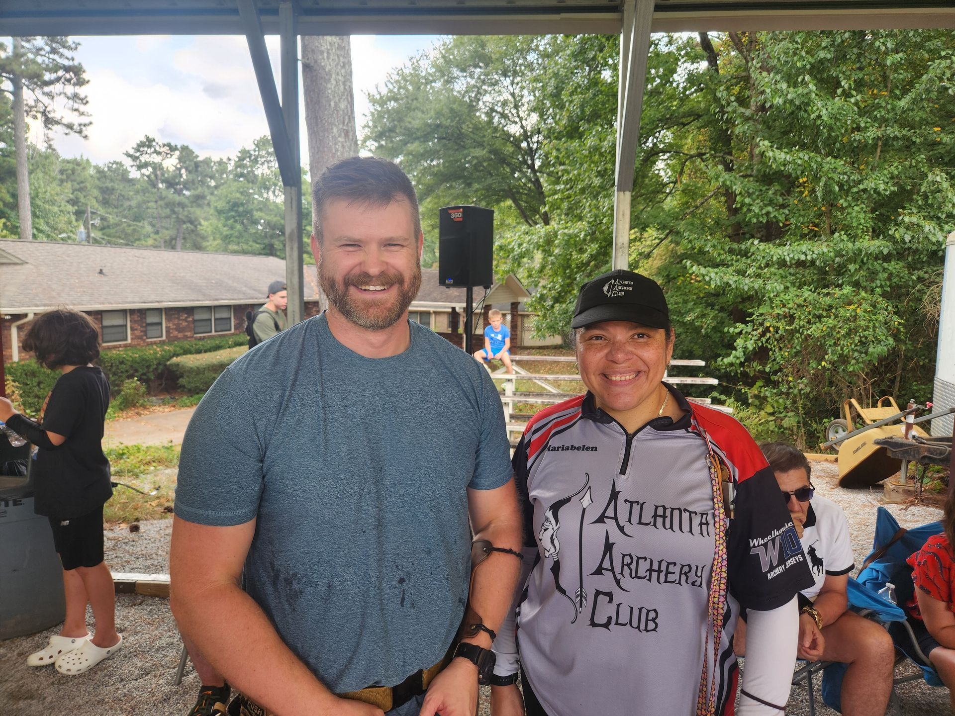 Two people smiling under a pavilion at an outdoor event, one holding a microphone.
