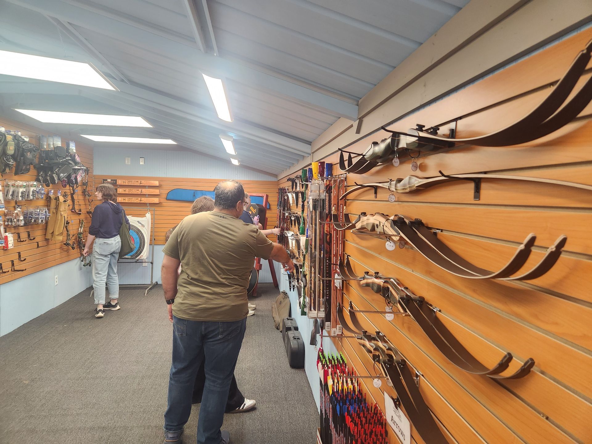 Two people browsing bows and archery gear in a brightly lit store aisle