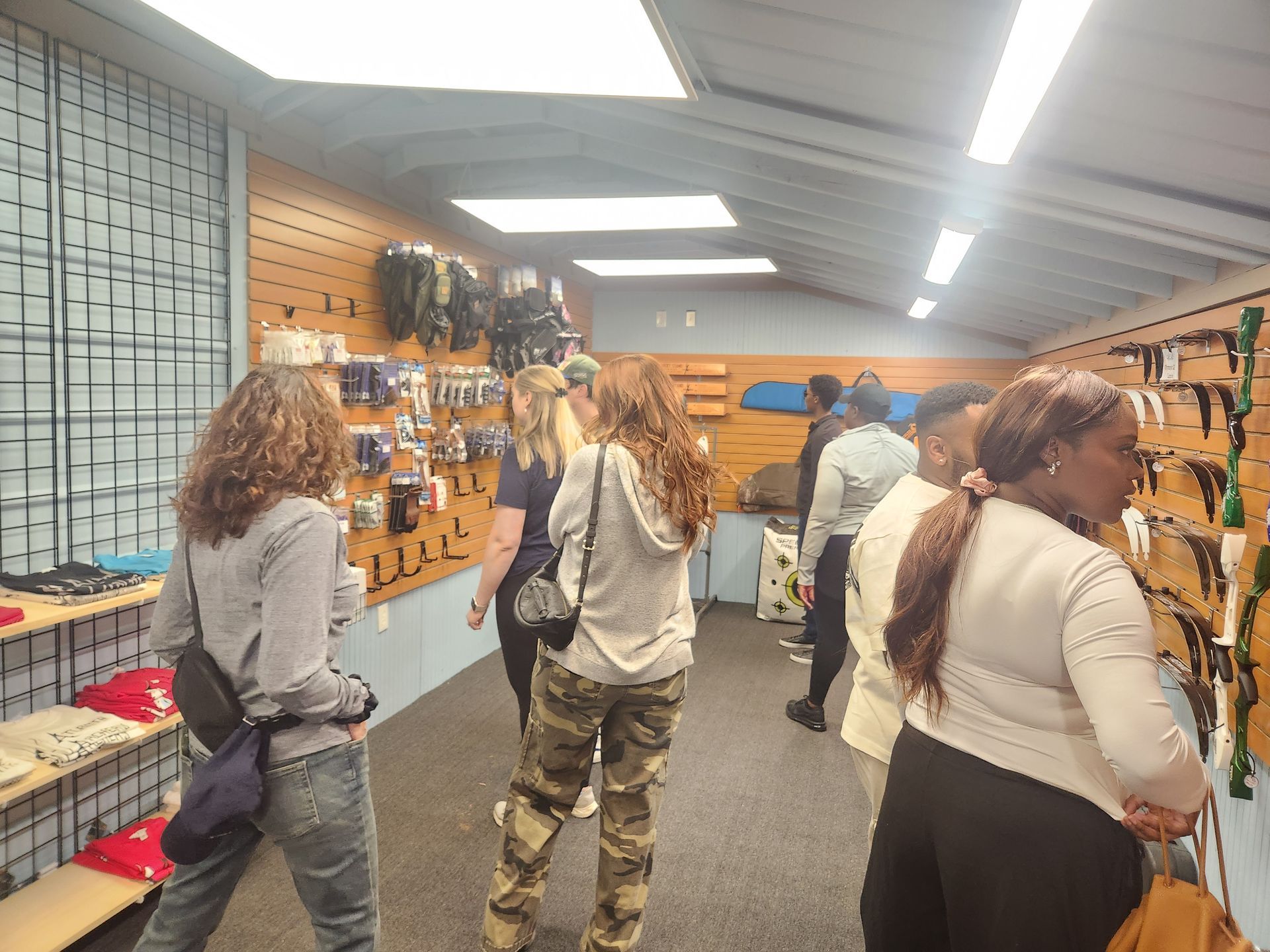 People browsing shelves in a narrow indoor store aisle with orange wall displays and bright ceiling lights