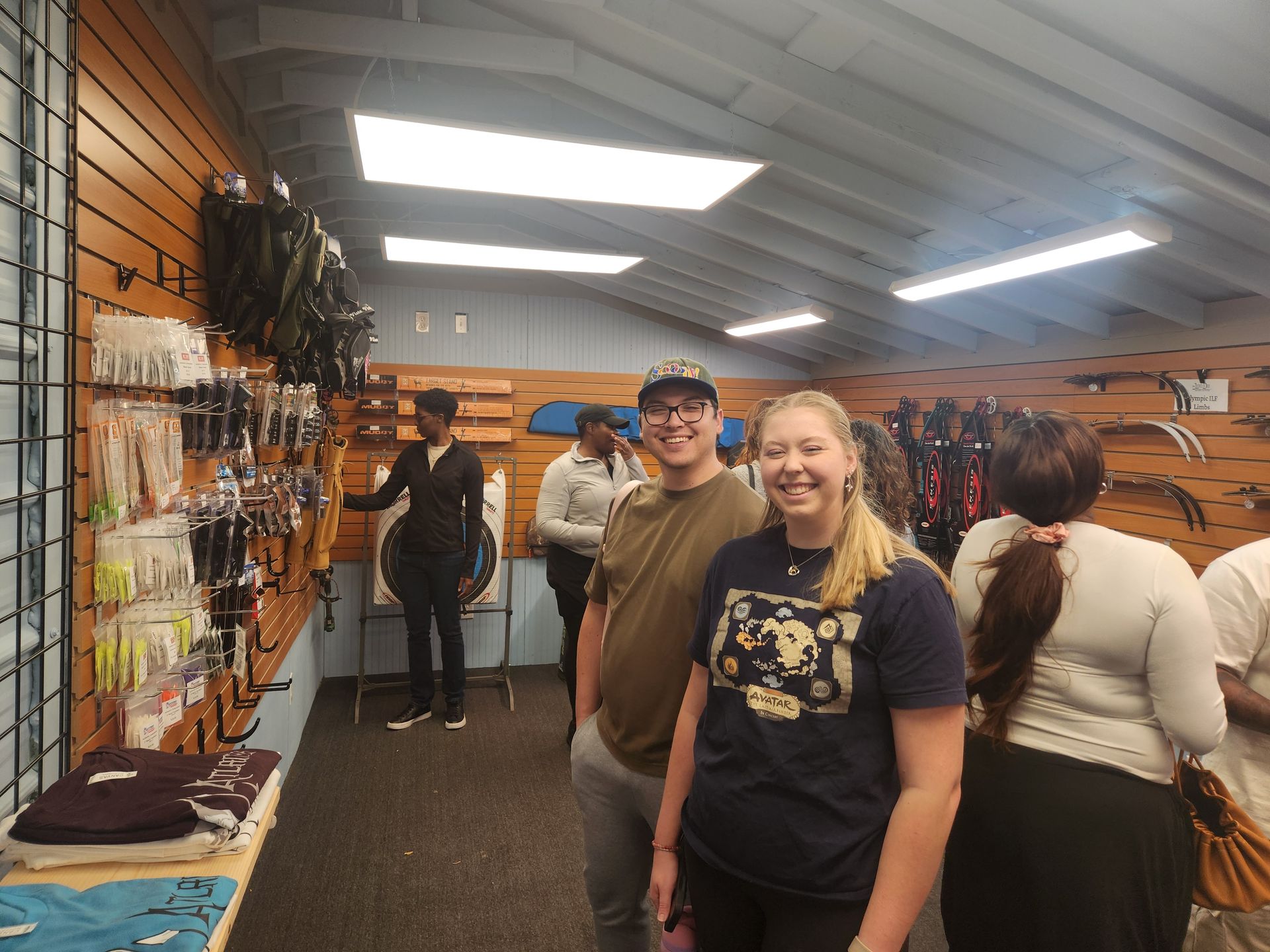 Smiling people in a brightly lit gear shop with racks of equipment along the walls