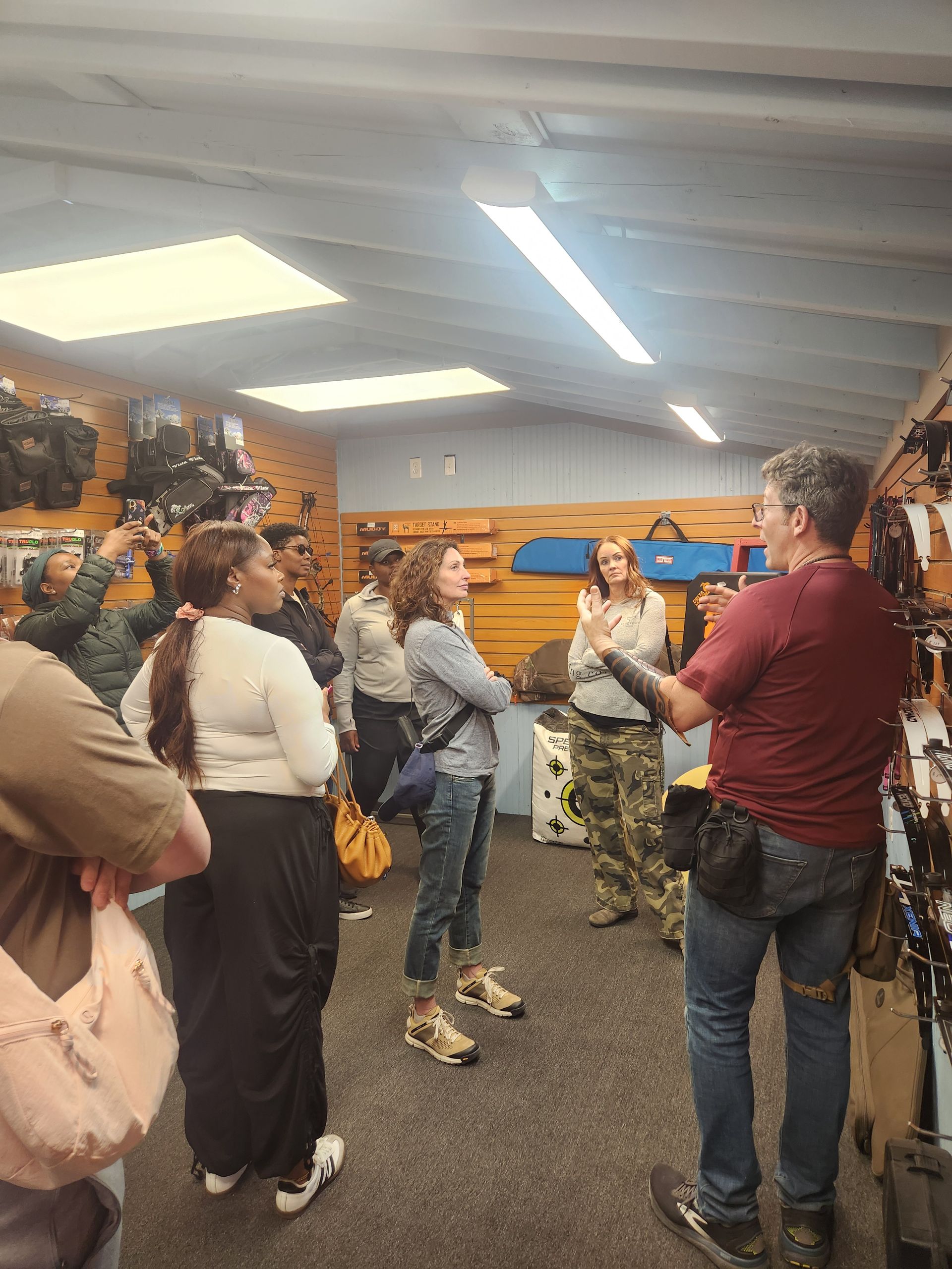 People gathered indoors in a wooden room, listening to a speaker near a wall map.