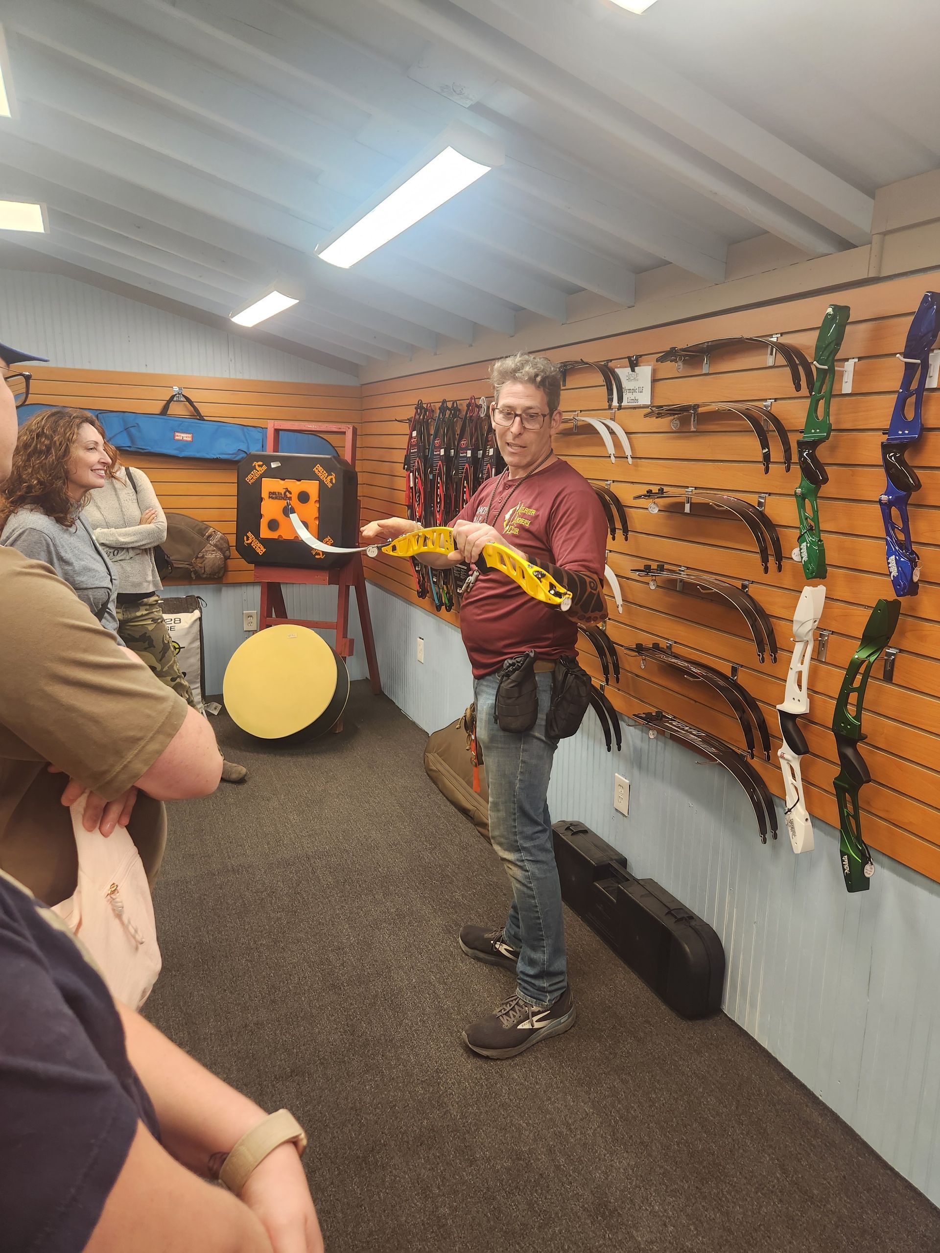 Person holding a yellow toy rifle in a brightly lit indoor archery range, with bows on the wall.