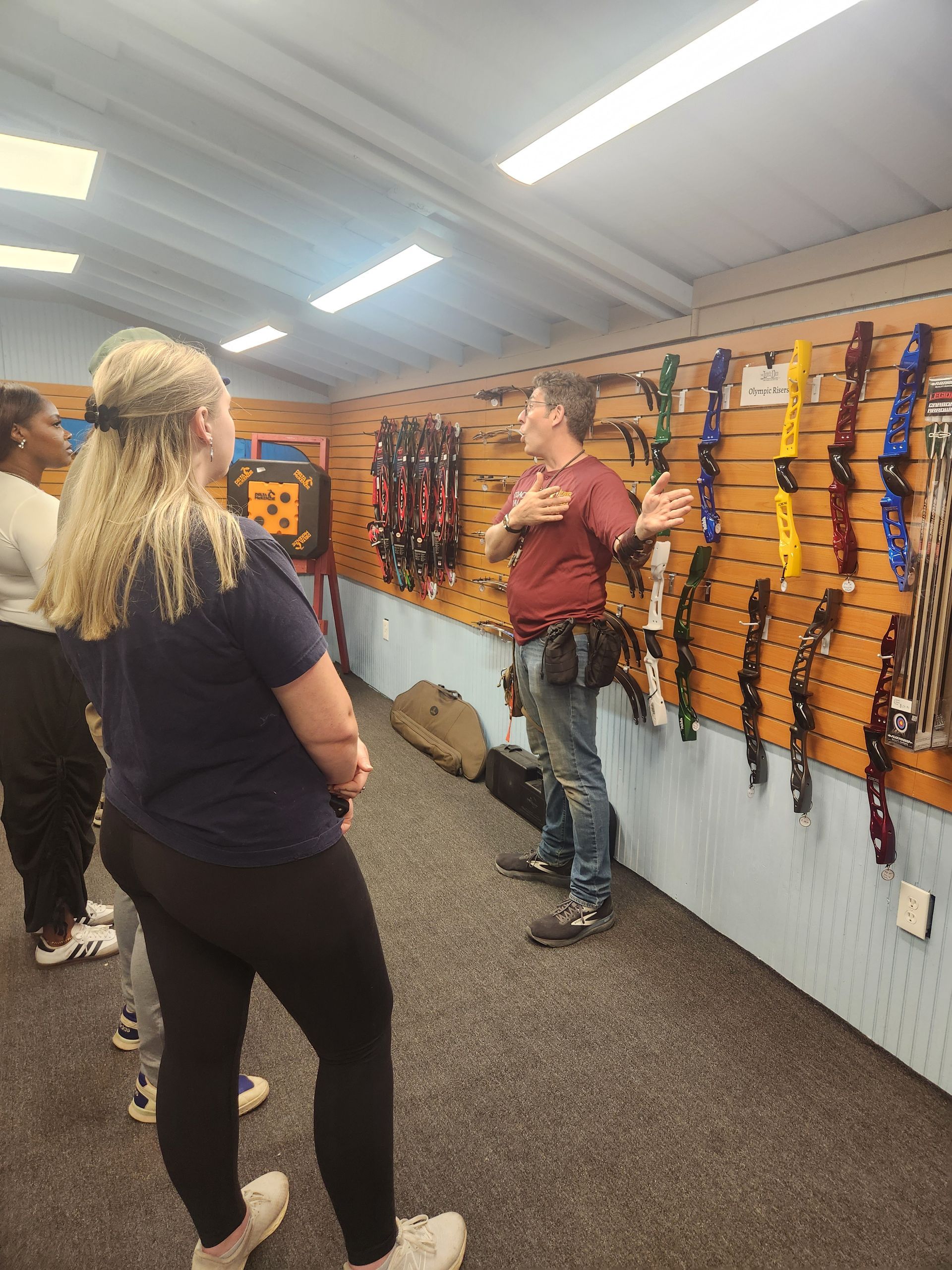 People standing in a gun range, looking at rifles displayed on a wall.