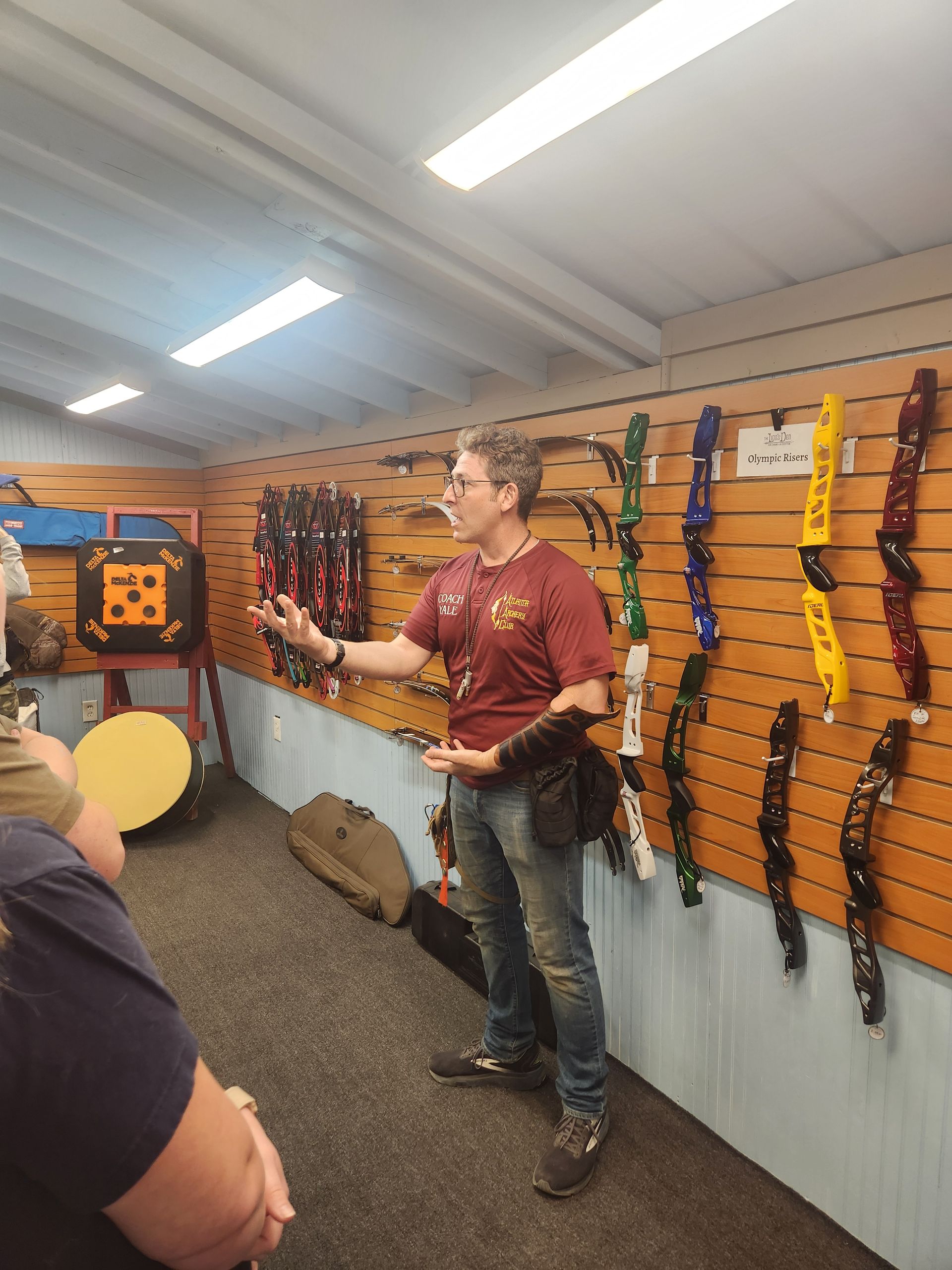 Person speaking in an indoor archery shop, with bows and equipment displayed on the wall.