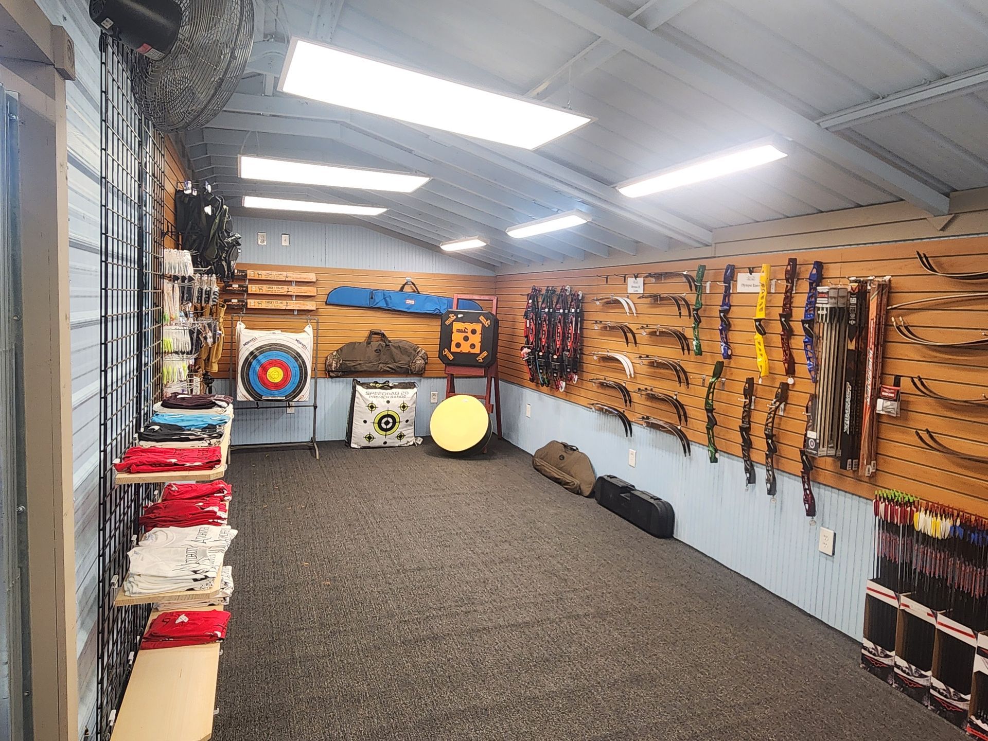 Indoor archery range with targets, bows on wall racks, and mats on the floor