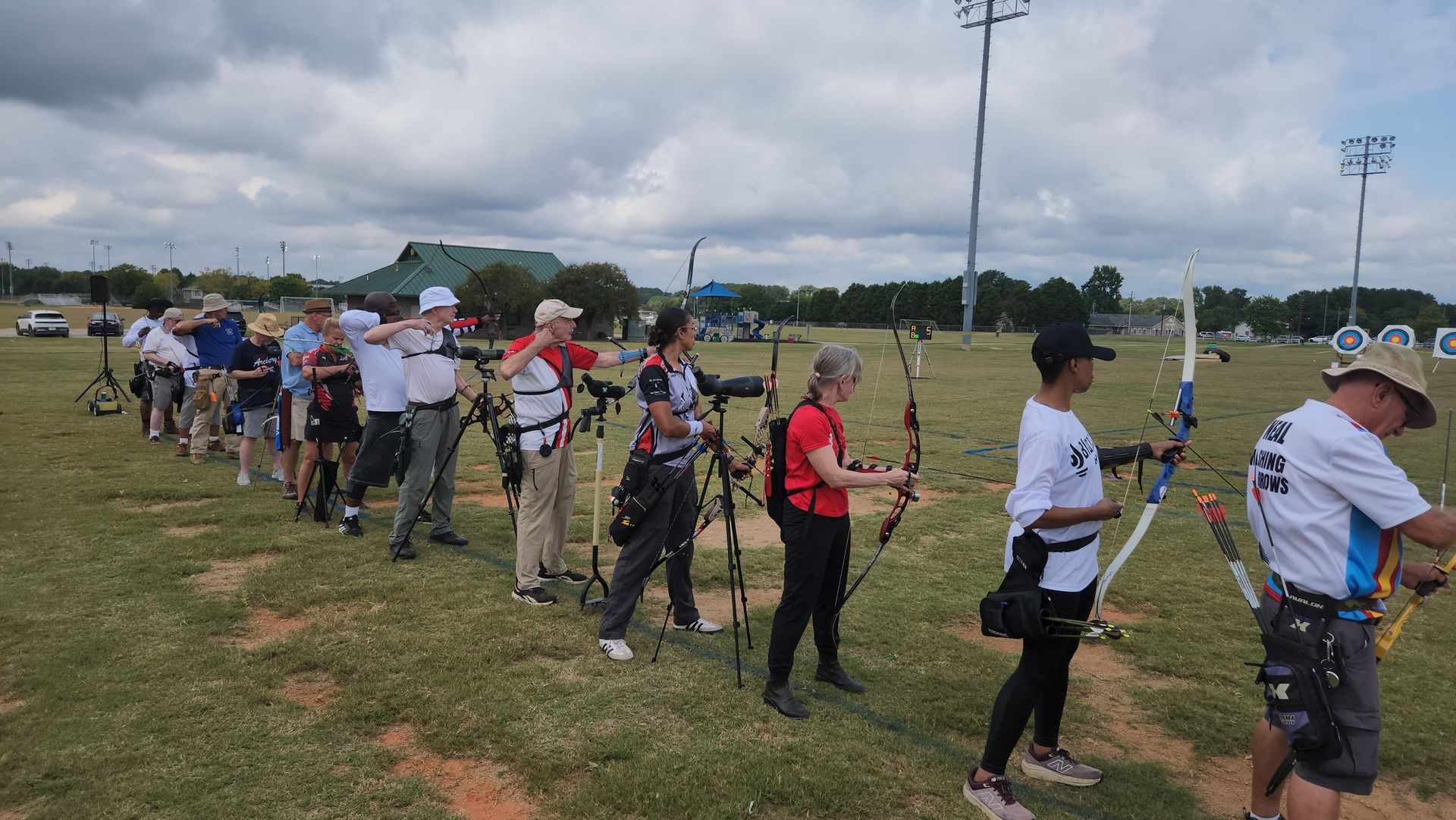 Group of senior people holding recurve and compound bows outdoors at an archery range