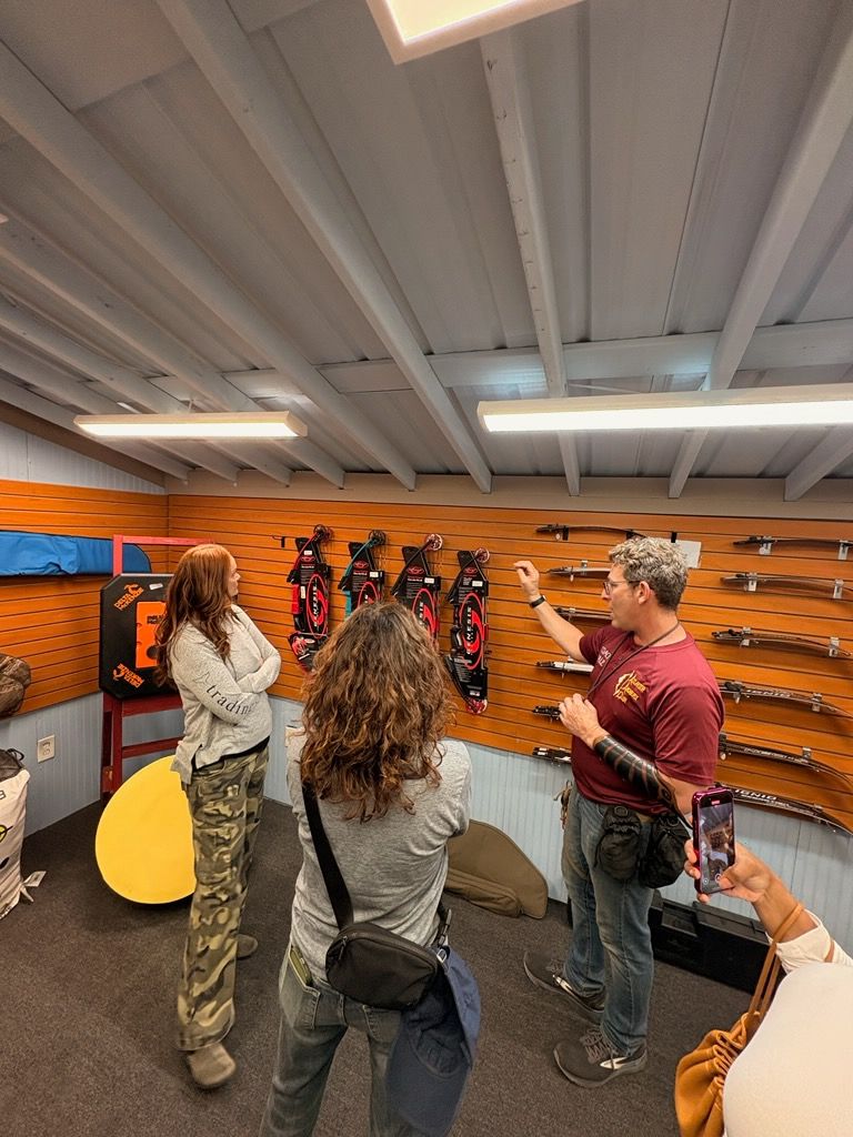 People in a cozy room with orange walls, looking at hanging items and pointing during a discussion.