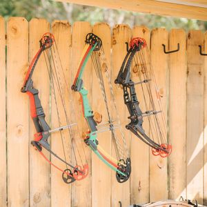 Three compound bows hanging on a wooden fence, various colors.