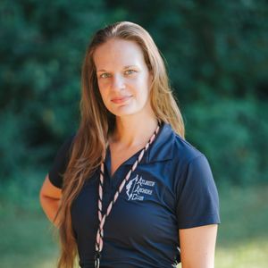 Woman in navy shirt with lanyard, smiling outdoors.