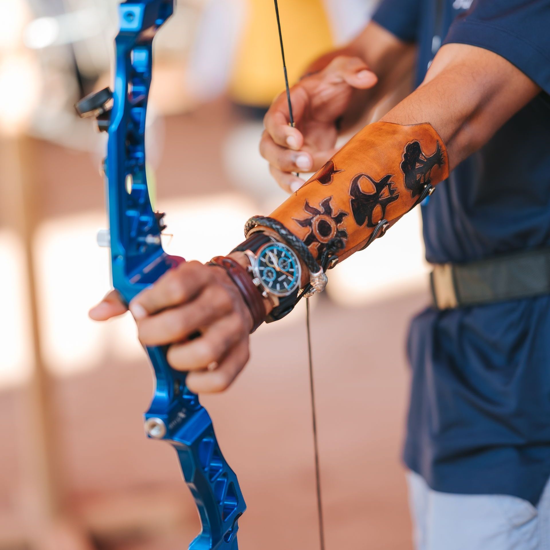 Person drawing back a blue bow, wearing a brown leather armguard with decorative carvings.