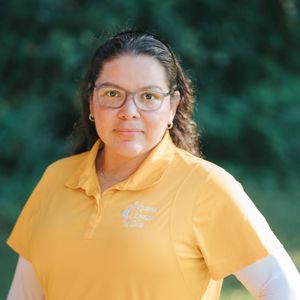 Woman wearing glasses and a yellow polo shirt, smiling outdoors.