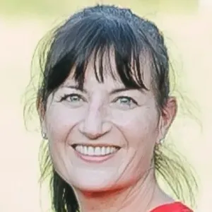Woman with dark hair smiling outdoors, wearing red shirt.